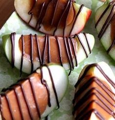 apples with chocolate drizzled on them sitting on a green plate next to a wooden table