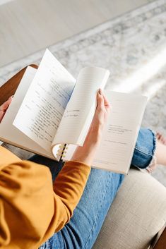 a person sitting on a chair holding an open book in their lap and reading it