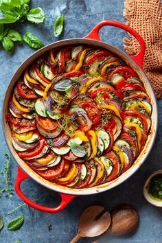 a pan filled with sliced up vegetables on top of a blue counter next to wooden spoons