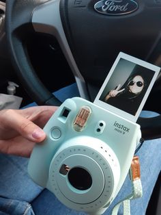 a person holding a polaroid camera in their hand while sitting in the driver's seat