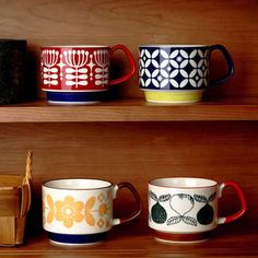 four coffee mugs are lined up on the shelves in front of a wooden box