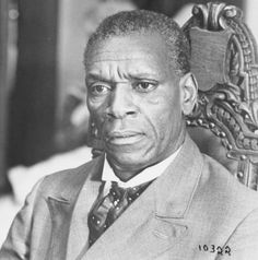 an old photo of a man in a suit and tie sitting in a chair with his head turned to the side