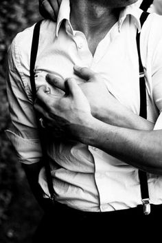 a man in suspenders is holding his hand on his chest