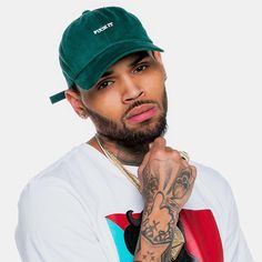 a man with tattoos wearing a green hat and holding his hand to his chin while looking at the camera