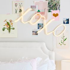 a white bed topped with lots of pictures next to a neon sign that says love