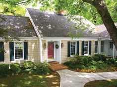 a white house with blue shutters and red door in the front yard is surrounded by trees