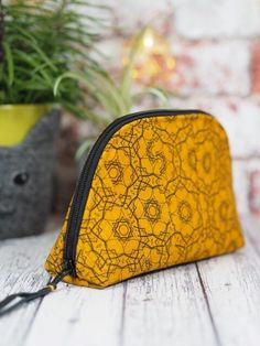 a yellow and black zippered pouch sitting on top of a wooden table next to a potted plant