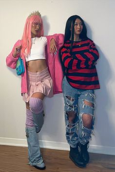 two women standing next to each other in front of a wall with ripped jeans and pink hair