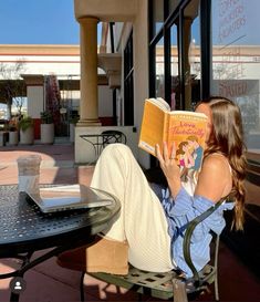 a woman sitting in a chair reading a book on a patio with a table and chairs