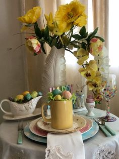 a table set for easter with yellow flowers in a vase and plates on the table