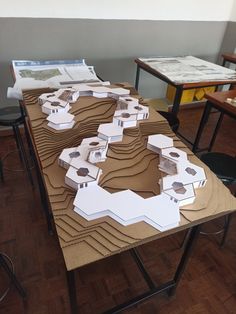 a table with some paper cut out of it on top of wooden flooring next to chairs and desks