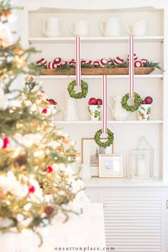 a christmas tree in front of a shelf with wreaths on it