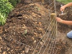 a woman kneeling down next to a fence with gardening tools in her hand and dirt on the ground