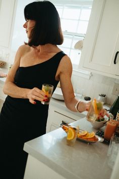 a woman standing in a kitchen holding a glass with orange slices on the counter top