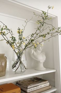 vases with flowers and books on a shelf in a white room, one is empty