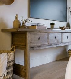 a tv is mounted on the wall above a wooden table with baskets and vases