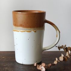 a white and brown coffee cup sitting on top of a wooden table next to dried flowers