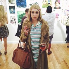 a woman in a striped dress and fur coat holding a wine glass while looking at the camera