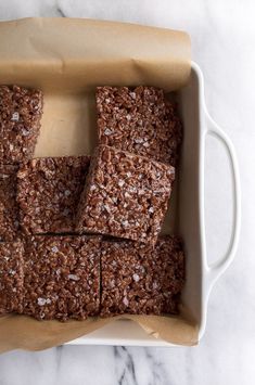 some brownies are in a white dish on a marble counter top and is ready to be eaten