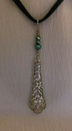 a black cord necklace with a silver pendant and green bead on it's end