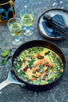 a pan filled with food next to two glasses