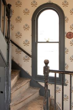 an open window sitting above a set of stairs next to a wall papered with flowers