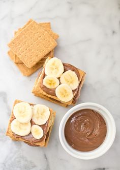 peanut butter and banana slices on crackers next to a bowl of nutella dip