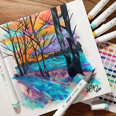 some watercolor pencils are laying on top of a drawing book with trees in the background