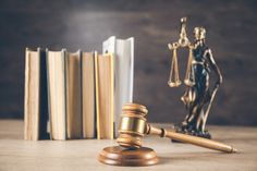 a judge's gavel next to books on a wooden table with a statue of lady justice in the background