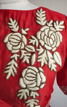 the back of a red dress with white flowers on it's chest and shoulders