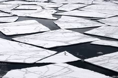 an aerial view of ice floes in the water and snow covered land, with one person walking on it