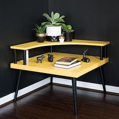 a corner table with books and plants on it in front of a black painted wall