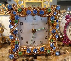 an ornate clock sits on a table next to other small clocks with different colored stones