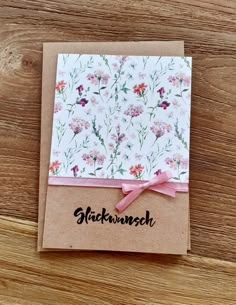 a greeting card with pink ribbon and floral print on it, sitting on top of a wooden table