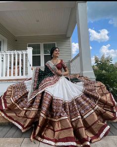 a woman is sitting on the porch wearing a dress with an elaborate skirt and headpiece