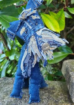 a stuffed animal made out of jeans on top of a rock in front of some trees