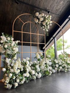 white flowers and greenery are arranged on the floor in front of an iron trellis