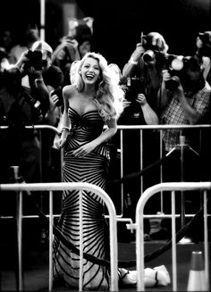 a woman standing in front of a crowd behind a metal barricade with cameras around her