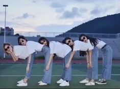 four women in white shirts and jeans posing on a tennis court