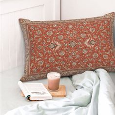 an orange pillow sitting on top of a bed next to a book and glass of milk