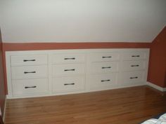 an empty room with white cabinets and wood flooring in the corner, along with a bed