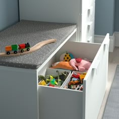 a toy train sits in the drawer of a white dresser next to a gray bed