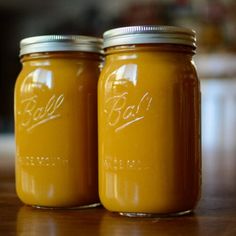 two jars filled with yellow liquid sitting on top of a wooden table next to each other