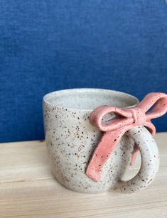 a ceramic cup with pink handles on a wooden table next to a blue wall,