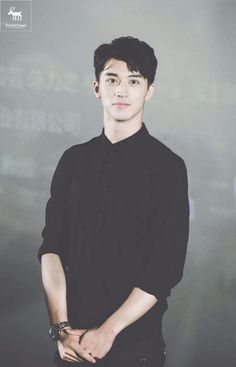 a young man standing in front of a chalkboard with writing on the wall behind him