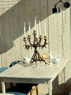 a wooden table topped with white candles and dishes next to a wall mounted light fixture