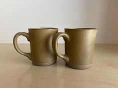 two coffee mugs sitting side by side on a wooden countertop, one is gold and the other is white