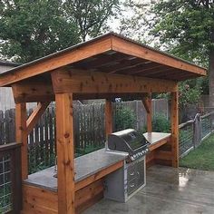 a wooden gazebo with benches and grills in the back yard, surrounded by trees