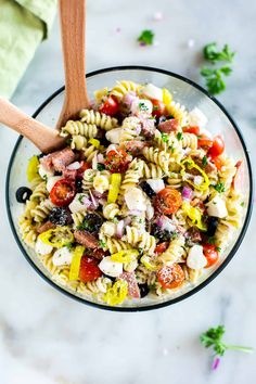 a bowl filled with pasta salad on top of a white marble counter next to a wooden spoon