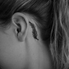 a woman's left ear has a feather tattoo on it